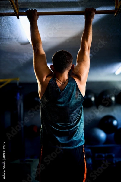 Fototapeta Back view of a strong man doing pull ups in a gym