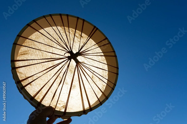 Fototapeta An image of a handmade leather meditation drum being held up against a bright blue sky. 