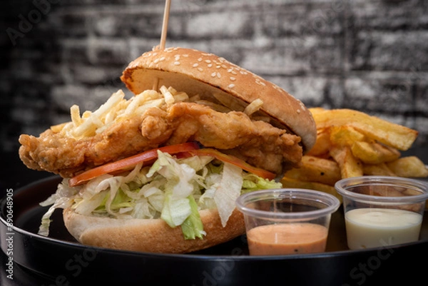 Obraz Crispy chicken burger on black background. Tomato, lettuce, chicken burger, sauces and fries.