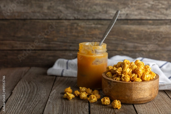 Fototapeta Sweet caramel popcorn in a bowl on a wooden background. Salted caramel popcorn. Caramel sauce. Close up. Topping. Place for text. Copy space