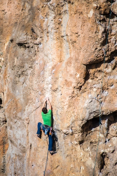 Obraz A rock climber climbs to the top along a difficult route.
