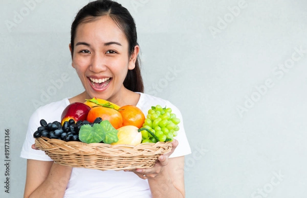 Fototapeta Young smiling woman posing with basket of fresh vegetables. Time of healthy food, bananas, apple, tomato, green grapes. Vegetables and Fruits.