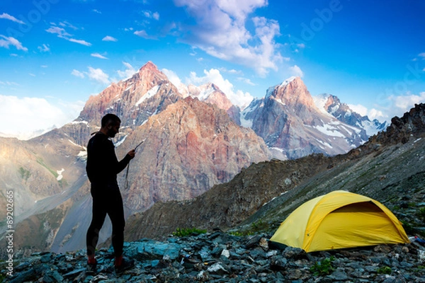 Obraz Explorer talking via radio station.
Silhouette of man in wild mountain landscape walk along yellow camping tent holding radio transmitter connection with team blue sky sunny evening