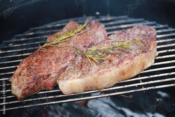 Fototapeta Grilled steaks topped with fresh rosemary on barbecue grill with char marks