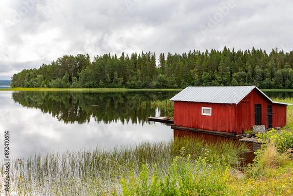 Fototapeta Red wooden pier on lake shore with reflection of trees on shore
