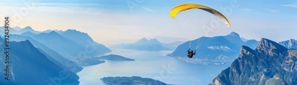 Fototapeta A man is flying a parachute over a beautiful mountain range and a lake