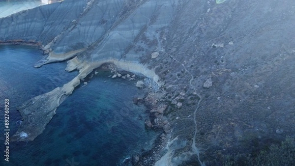 Fototapeta Tat-Tonn or Spritzing rock, snorkeling point between Qarraba Bay and Ta'Babu Cove, Ghajn Tuffieha, Mgar, Malta. Aerial view of the emerald sea and rocky coast in early morning still in the shade of