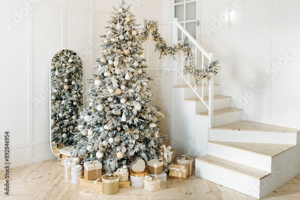 Obraz Beautifully adorned Christmas tree with gold and white presents, positioned next to a staircase with festive garlands. The mirror reflects the warm, cozy atmosphere