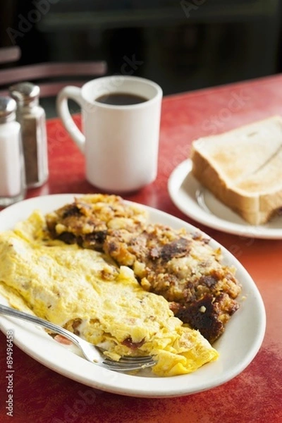 Fototapeta Bacon and Tomato Omelet Served with Hash on a White Plate; Coffee and Toast on a Diner Table
