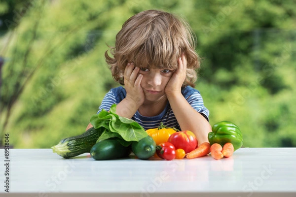 Obraz Cute little boy sitting at the table, unhappy with his vegetable meal, bad eating habits, nutrition and healthy eating concept