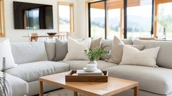 Fototapeta A stylish gray living room featuring a sectional sofa adorned with pillows, a wooden coffee table, and a large TV on the wall, creating a comfortable and modern space.