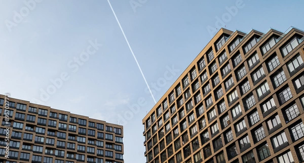 Fototapeta A trace of a passing plane over a modern multi-storey business class building.