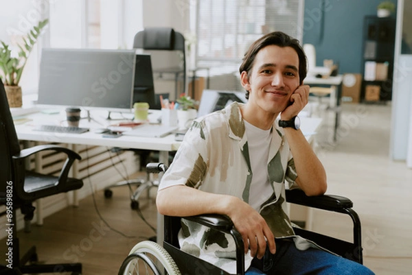 Fototapeta Portrait of smiling Caucasian IT specialist with disability looking at camera while his head based on hand, he in office of modern high-end IT company