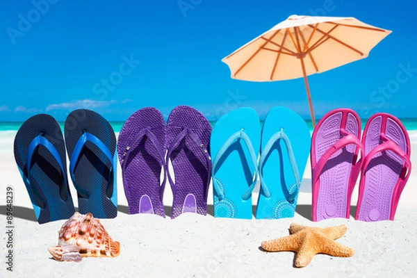 Fototapeta Bunte Flip Flops in einer Reihe mit Muscheln und Sonnenschirm