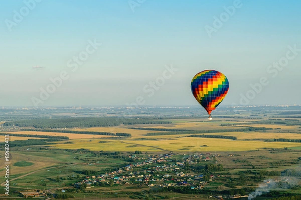 Fototapeta Colorful hot air balloon flying over the village, forest and fields