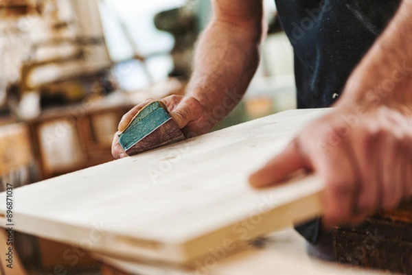 Fototapeta Carpenter sanding wood using sandpaper in workshop