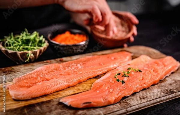 Fototapeta Fresh trout salmon filet with herbs greens on wooden board and chief hands on blurred background. Omega orange fish with rosemary for healthy nutrition
