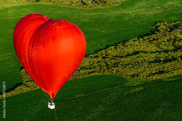 Fototapeta Red balloon in the form of heart over green fields and forests