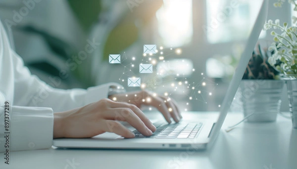 Fototapeta Close-up of hands typing on a laptop, with email icons floating above, symbolizing digital communication and productivity.