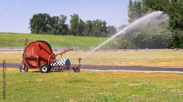 Obraz Traveling sprinkler hose reel irrigation machine watering a park field.