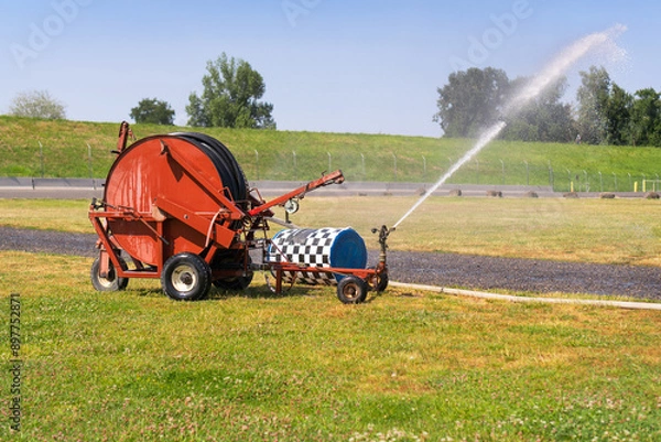 Obraz Traveling sprinkler hose reel irrigation machine watering a park field.