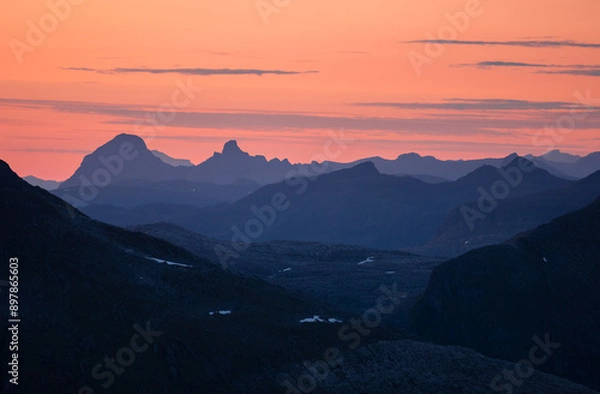 Fototapeta Midnight sun in arctic summer landscape of Norway. Silhouettes of mountain ranges in sunset colours of blue, orange and purple. Few clouds on clear dawn and dusk sky. Moody mountain range landscape
