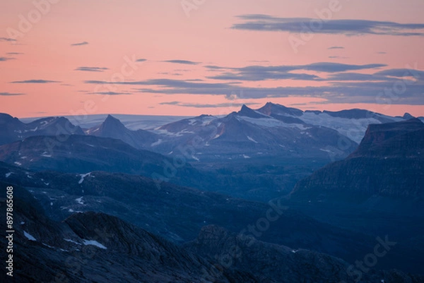 Fototapeta Midnight sun in arctic summer landscape of Norway. Silhouettes of mountain ranges in sunset colours of blue, orange and purple. Few clouds on clear dawn and dusk sky. Moody mountain range landscape