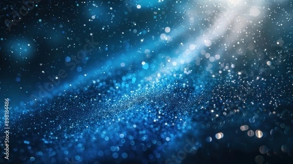 Fototapeta A scene of ethereal enchantment is created against the backdrop of darkness by the gentle descent of blue glitter particles in the light rays, captivating everyone in sight.