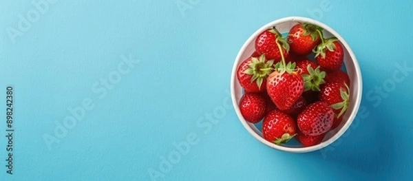 Fototapeta Delicious berry dessert featuring fresh ripe strawberries in a cup on a blue paper background viewed from the top with copy space image