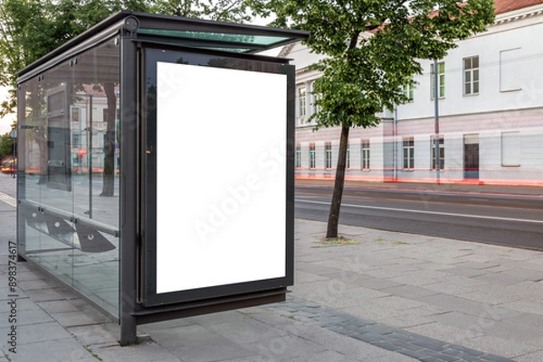 Fototapeta Blank White Bus Stop Vertical Poster Billboard Mockup On An Empty City Street. Advertising Lightbox On The Sidewalk With Car Light Trails In The Background