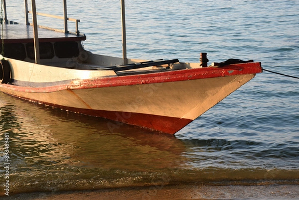 Fototapeta Boats on the edge of a clean beach, the rays of the setting sun