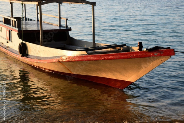 Fototapeta Boats on the edge of a clean beach, the rays of the setting sun