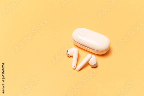 Obraz Close-up of wireless earbuds with charger case on pastel yellow background.