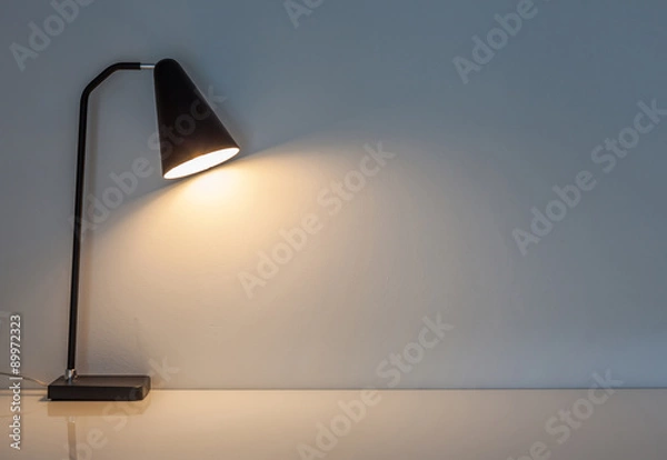 Fototapeta Nowoczesna lampa biurka oświetla na tle ściany.