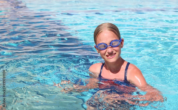 Fototapeta A girl in swimming glasses swims in a pool at a resort on a summer sunny day. Summer travel hotel vacation or classes