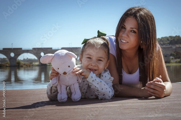 Fototapeta Madre e hija acostadas en el embarcadero. Una niña y su mama disfrutando del verano junto al rio. Madre joven soltera.
