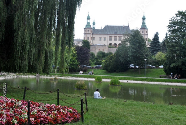 Fototapeta człowiek siedzący na trawie nad rzeką w parku z zamkiem w tle