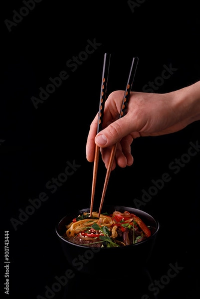 Obraz Stir fry noodles with vegetables and shrimps in black bowl. Slate background. Top view. Copy space.