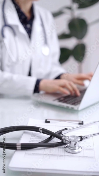 Fototapeta Stethoscope is lying on the glass table while doctor woman is working with laptop computer on the background. Medicine and pharmacy concept