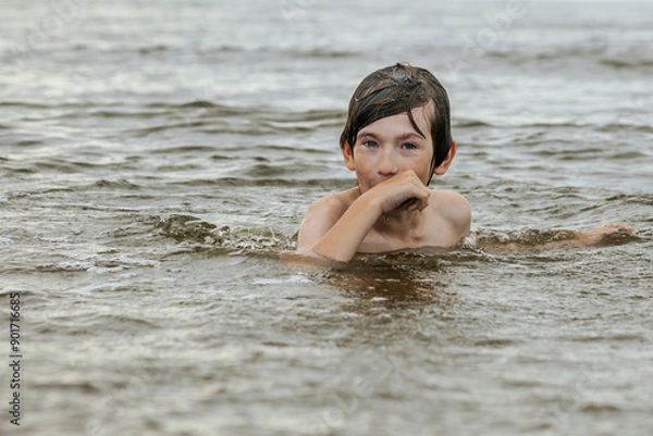 Fototapeta A young child struggling and shouting in the water, appearing to be in distress, with splashes around him and a vast expanse of water in the background. The scene evokes a sense of urgency and concern