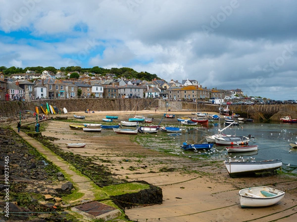 Fototapeta Fishing and sailing boats moored at low tide in harbour at Mousehole, a fishing port in Penzance on the shore of Mount's Bay in Cornwall, England. Cloudy sky. Text space.