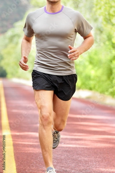 Obraz Low section of determined man running on country road. Young male is in sports clothing. He is representing fit and healthy lifestyle.