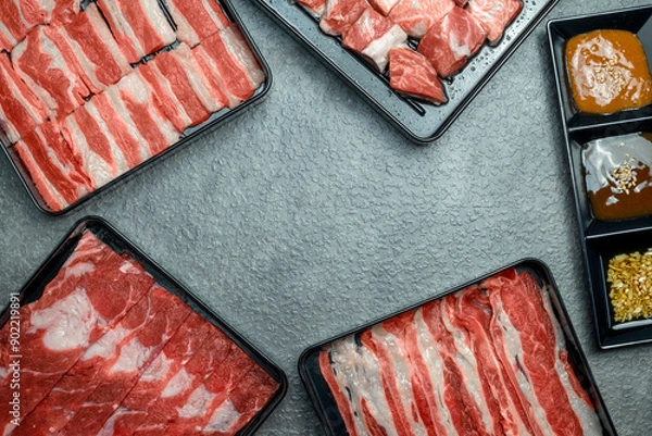 Fototapeta A variety of meats are displayed in plastic containers on a grey surface