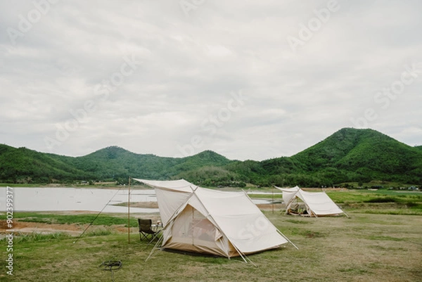 Fototapeta White camping picnic tent campground in outdoor park lake with mountains and blue sky with white clouds in the background. Adventure travel and vacation concept
