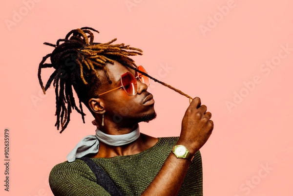 Obraz Portrait of a young man in green with dreadlocks and blue sunglasses, isolated on pink