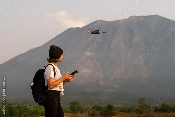 Fototapeta A girl of European appearance, a traveler with a backpack, shoots a video with a drone, against the backdrop of beautiful mountains.