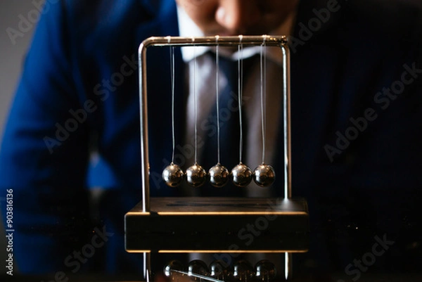 Obraz Unrecognizable businessman pulling small metal ball of Newton cradle and observing momentum over glass tabletop