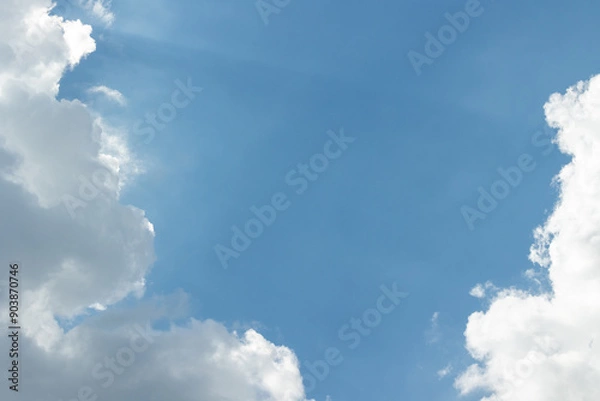Obraz White clouds in a blue sky with sunbeams breaking through them