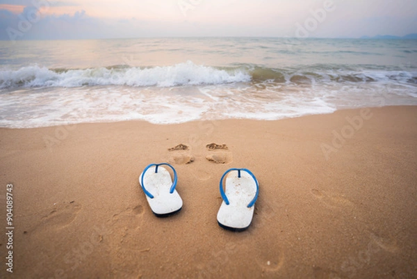 Fototapeta White sandals on the beach in the morning, the sea with white waves.