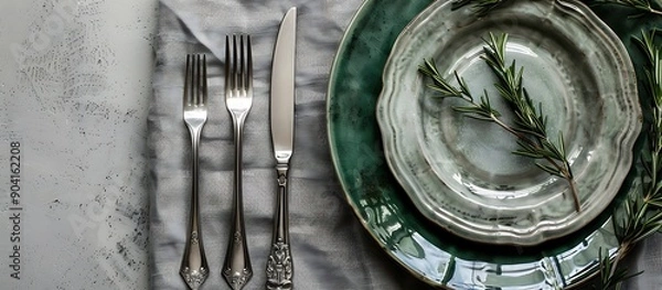 Fototapeta Top view of grey linen napkin with silver cutlery, green ceramic plates, rosemary sprigs, concrete background, high resolution photo.